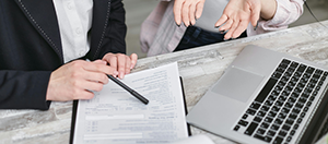 person holding pen on paper with hands over laptop